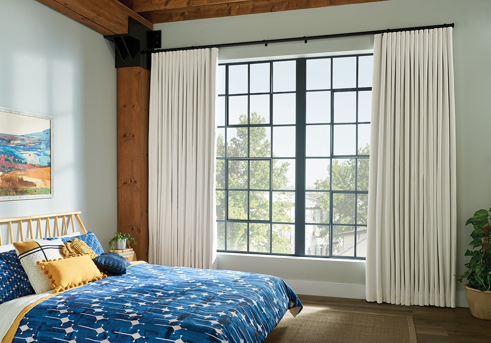 Neutral-colored curtains hanging in a cozy, well-lit bedroom with soft bedding and natural light filtering through the window.