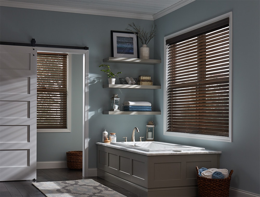 Wood blinds hanging above a bathtub letting light in.